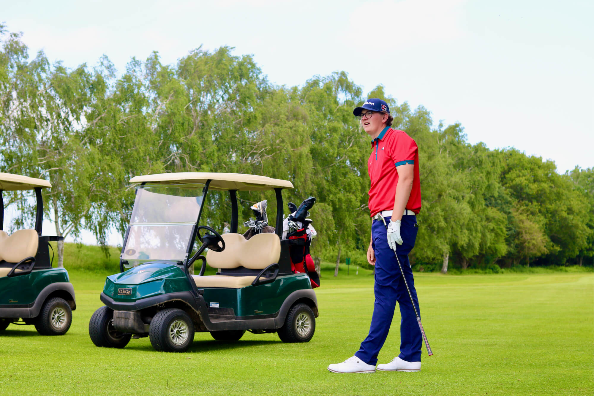 Robbie standing on the golf course with 2 green golf carts beside him